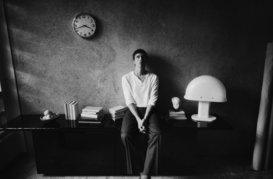 Photograph a person sitting in a room with a wall having a clock